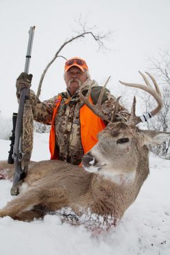 Hunter L.P. Brezny with muzzleloader rifle and freshly downed swamp buck in the Minnesota snow.