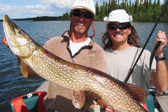 Two fishermen, one with a massive Canadian pike from Wollaston Lake, the other with a fishing rod.