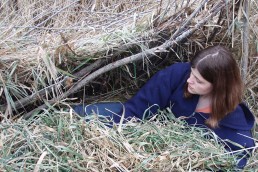 Woman in a makeshift grass survival shelter.